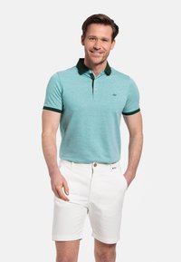  Lichtblauw poloshirt met een donkergroene kraag en mouwaccenten, gecombineerd met witte shorts. Glad materiaal met een subtiele textuur.