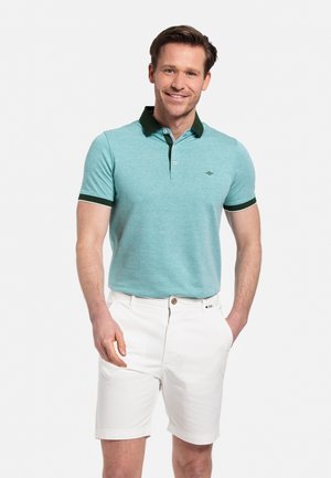 Lichtblauw poloshirt met een donkergroene kraag en mouwaccenten, gecombineerd met witte shorts. Glad materiaal met een subtiele textuur.