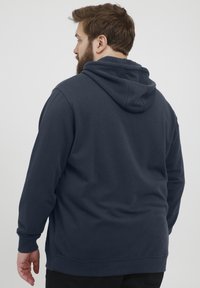Sudadera azul marino con capucha ajustable, mangas largas, puños acanalados y corte relajado. Tejido de mezcla de algodón con una textura suave.