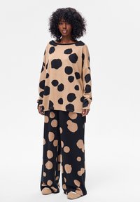 Beżowy oversize sweter z dużymi czarnymi kropkami, zestawiony z czarnymi luźnymi spodniami w beżowe kropki. Miękka faktura z szerokimi rękawami.