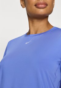 Μωβ αθλητική μπλούζα με στρογγυλή λαιμόκοψη, κοντά μανίκια, υφασμάτινη υφή και μικρό λευκό λογότυπο Nike στο στήθος.