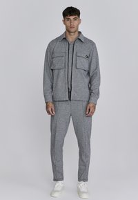 Jachetă și pantaloni asortați, gri, cu un textură, având două buzunare la piept, închidere cu fermoar și teniși albi. Design minimalist cu o formă ajustată.
