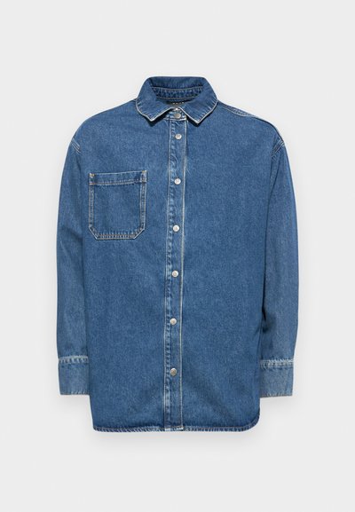 Blå denimskjorte med knappelukking foran, krage og lomme på venstre bryst. Har lange ermer og synlige sømmer.