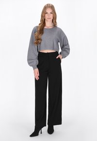 Pulover gri scurt cu maneci tip balon, combinat cu pantaloni negri cu picioare largi. Modelul pozează cu o mână în buzunar, purtând botine negre cu toc.