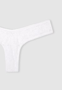 String in pizzo bianco con motivo floreale, caratterizzato da una vita sottile e bordi testurizzati. Il tessuto semitrasparente mette in risalto il design delicato.
