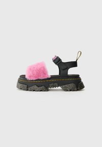 Kraftige svarte sandaler med rosa kunstpels på toppen, justerbar stropp og spraglete teksturert såle. Har gult søm og en løftripe.