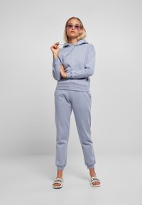 Sudadera azul claro y joggers a juego, fabricados en una suave mezcla de algodón, con puños acanalados y capucha ajustable con cordón. Acentuados con chanclas con eslogan.