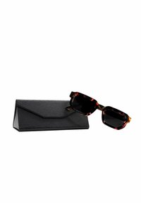 Occhiali da sole tartarugati con lenti nere e montatura robusta, esposti accanto a un astuccio nero con texture e chiusura a patta.