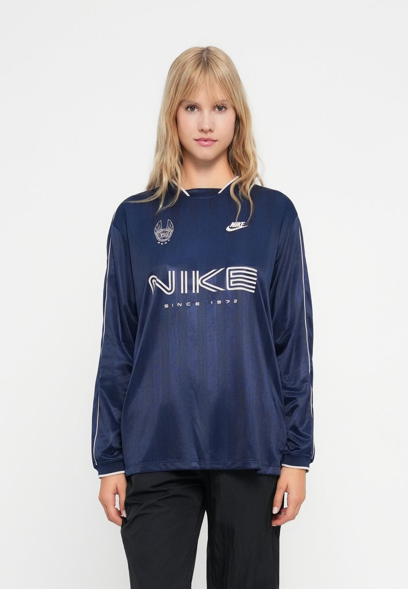 Morska plava majica dugih rukava Nike s okruglim izrezom, bijelim logotipom i prugastim naglascima na rukavima; napravljena od glatkog, laganog materijala.