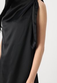 Svart satin klänning med en draperad design och en knuten axeltermos, som betonar slanka linjer och minimalistisk stil.