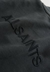 Juodas megztinis su tekstūrine siuvinėjimu, rašančiu "ALSAINTS." Minkšta medžiaga, laisvas siluetas ir apvalus kaklas. Subtilus blizgesys paviršiuje.