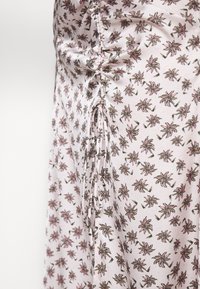 Gros plan d'un tissu rose avec un petit motif de palmier et un froncement latéral noué avec un cordon fin.