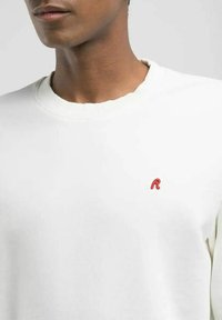 Felpa bianca in cotone, con collo rotondo e un piccolo logo 'R' rosso sul petto. Tessuto liscio, design casual.