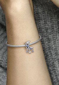Silver bangle bracelet featuring a crescent moon charm with decorative stars, adorned with blue and clear stones, on a textured arm.