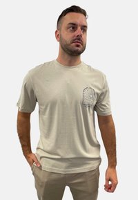 Hellgrau, kurzärmliges T-Shirt aus Baumwolle mit einem kleinen schwarzen Grafikdesign auf der linken Brustseite. Lässige Passform mit Rundhalsausschnitt.
