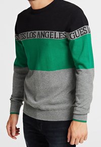 Maglione lavorato a maglia con scollo rotondo, caratterizzato da pannelli neri, verdi e grigi. Logo "Guess Los Angeles" in grigio sul petto.