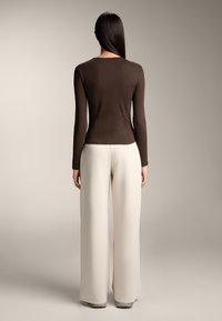 Brown fitted long-sleeve top with ribbed texture, paired with high-waisted, wide cream trousers with a vertical rib pattern. Neutral background.
