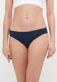 Șorturi de baie de culoare bleumarin, confecționate dintr-un material neted, cu un croi jos și o acoperire minimă, având un detaliu discret cu logo pe lateral.