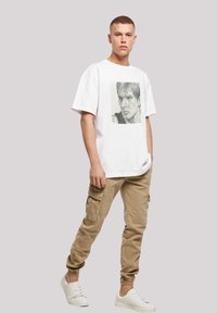 Hvid bomulds t-shirt med sort-hvid grafisk print, parret med beige cargo bukser med sidelommer og elastiske manchetter. Hvide sneakers.