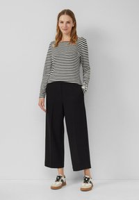 Zwart-wit gestreepte long-sleeve top, gecombineerd met brede zwarte broek en crèmekleurige sneakers met zwarte accenten en bruine zolen.