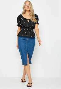 Schwarzes Oberteil mit Puffärmeln und floralem Stickereimuster, tailliert; kombiniert mit einem Denim-Bleistiftrock mit einem Schlitz vorne. Schwarze Flip-Flops.