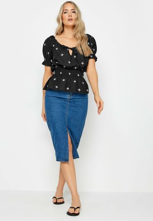 Top nero con maniche a sbuffo e ricami floreali, vita cinchata; abbinato a una gonna a tubo in denim con spacco frontale. Infradito nere.
