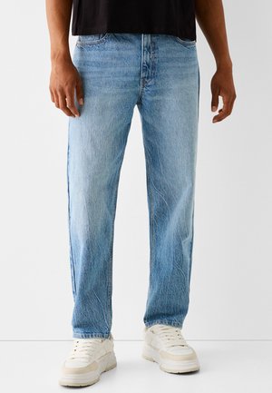 Jeans de mezclilla azul claro con un corte recto. Presentan un sutil desgaste y detalles de costura, combinados con zapatillas blancas para crear contraste.