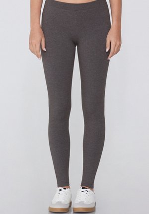 Leggings grigi realizzati in un tessuto elasticizzato con una superficie liscia, dotati di una vita alta, che si estendono fino alle caviglie, abbinati a sneaker bianche.