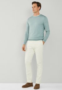 Himmelblauer Pullover mit langen Ärmeln, cremefarbene Hose und braune Wildlederschuhe. Glatte Textur, runder Ausschnitt, taillierter Schnitt. Schlichte und neutrale Farbpalette.
