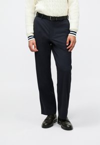 Ναυτικά παντελόνια με ίσια γραμμή, φτιαγμένα από ομαλό ύφασμα. Διαθέτουν ζώνη με θηλιές και συνδυάζονται με μαύρες slip-on παντόφλες.