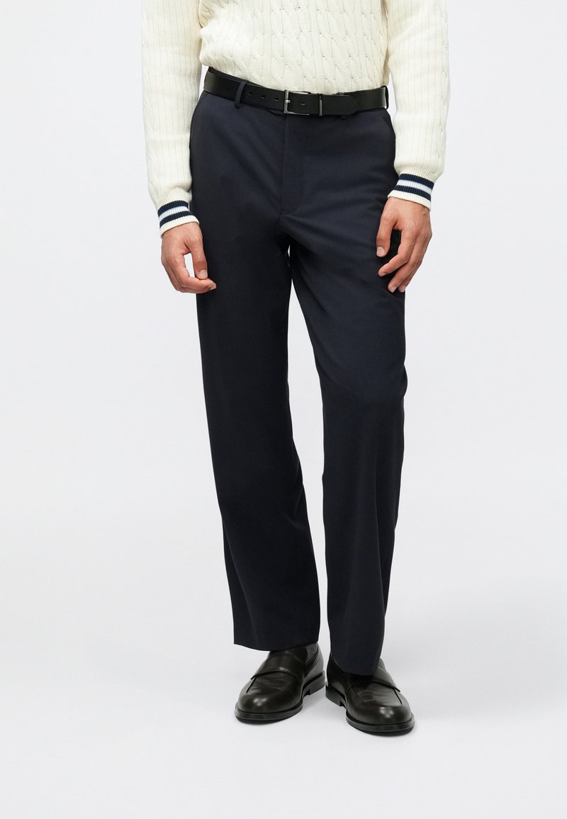 Ναυτικά παντελόνια με ίσια γραμμή, φτιαγμένα από ομαλό ύφασμα. Διαθέτουν ζώνη με θηλιές και συνδυάζονται με μαύρες slip-on παντόφλες.