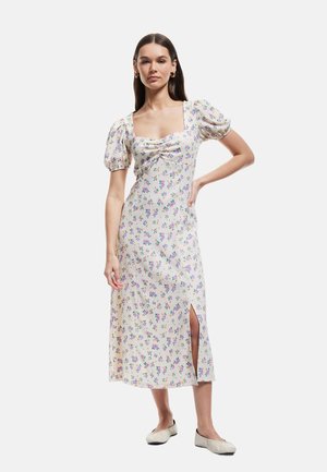 Robe midi florale avec manches bouffantes, décolleté carré et fente sur le côté. Fabriquée en tissu léger, elle présente une base blanche ornée de fleurs multicolores.