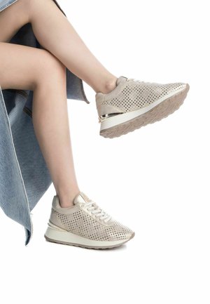 Zapatillas metálicas beige con parte superior perforada, cierre de cordones y una suela elevada en blanco roto con un acento dorado en la parte trasera.