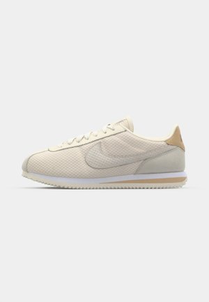 Beige verkkoakun sneaker, jossa on teksturoitu pinta, kermaiset nauhat, vaaleanharmaa mokkatee ja valkoinen kumipohja, jossa on sahalaitakuviot.