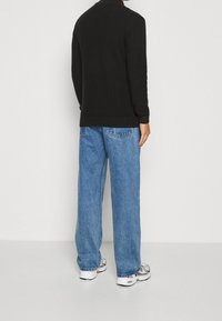 Zwarte lange mouwtrui met geribbeld textuur, gecombineerd met lichtblauwe wijde jeans en witte sneakers met zilveren accenten.