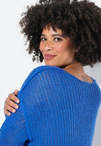 Maglione blu lavorato a maglia con un design a trama larga e aperta. Presenta un collo ampio e un tessuto texturizzato, che mette in mostra uno stile casual.