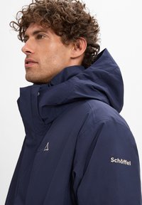 Marineblaue Kapuzenjacke mit strukturiertem Finish. Verfügt über ein Logo auf der Brust, einen hohen Kragen und einen lässigen Schnitt für den Einsatz im Freien.