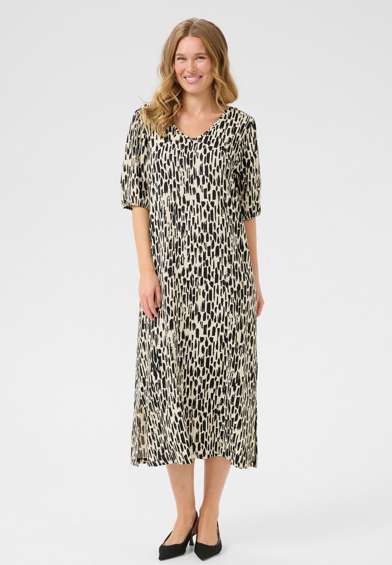 Midi dress in beige with black abstract pattern, short puff sleeves, V-neckline, and side slit. Accompanied by black pointed-toe shoes.