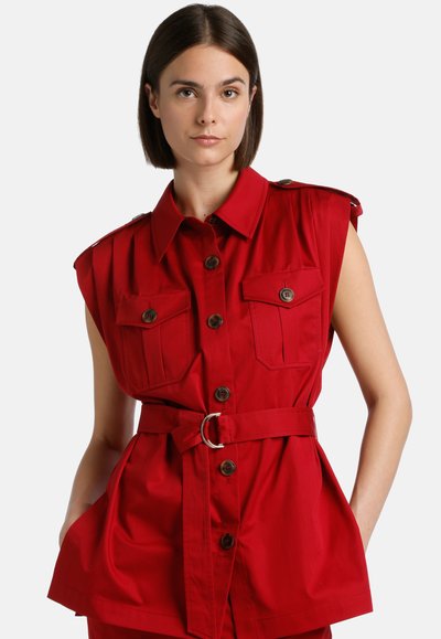 Red sleeveless shirt dress with button front, two chest pockets, shoulder pads, and belted waist. Smooth fabric with a structured shape.
