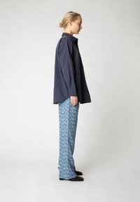 Marineblaues Übergrößenhemd mit langen Ärmeln, kombiniert mit blauen gemusterten weiten Hosen. Weiche Textur, Knopfdetails am Hemd und braunes Schuhwerk.