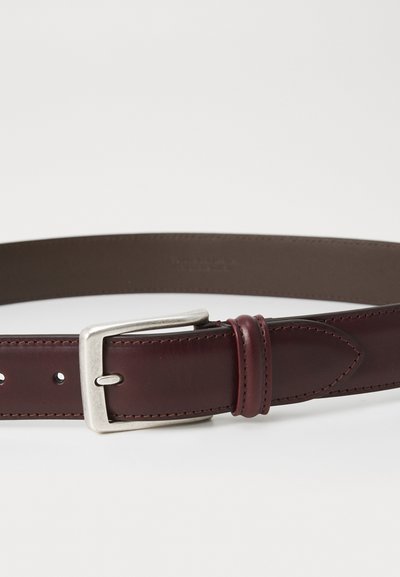 Cinturón de cuero en un burdeos oscuro con hebilla de metal plateado. Presenta una textura suave, costuras reforzadas y cinco agujeros ajustables.