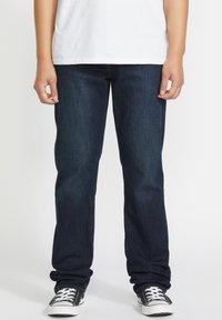 Vaqueros de mezclilla azul oscuro con un corte recto, que cuentan con un diseño clásico de cinco bolsillos y detalles de costura sutiles. Acompañados de zapatillas negras.