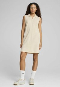 Beige ärmlös polo klänning med en strukturerad randig design, med krage och rak skärning. Matchad med vita strumpor och beige sneakers.