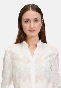 White blouse featuring a subtle floral pattern, lightweight fabric, a mandarin collar, and front button closure.