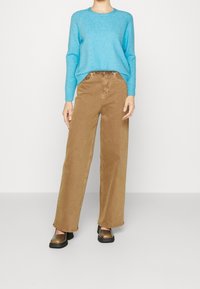 Light blue knit sweater paired with loose brown wide-leg pants and dark slip-on shoes. Smooth texture and relaxed fit.