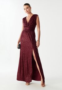 Burgundia säättöta kleit sügava V-dekolteega, ümber mähitud disainiga, külgsuise ja sädelevate tekstuuridega. Kombineeritud väikese musta käekotiga ja rihmadega sandaalidega.