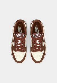 Par čokoladno-bijelih Nike tenisica s vezicama viđenih odozgo na bijeloj pozadini.