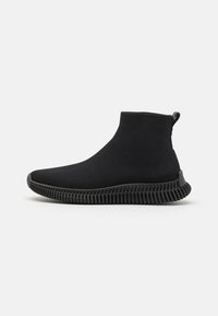 Schwarze, gestrickte Schuhe in Knöchelhöhe mit einer strukturierten Oberfläche, gummierter Sohle mit Rillen und einem Zugband hinten für einfaches An- und Ausziehen.