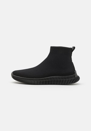 Schwarze, gestrickte Schuhe in Knöchelhöhe mit einer strukturierten Oberfläche, gummierter Sohle mit Rillen und einem Zugband hinten für einfaches An- und Ausziehen.
