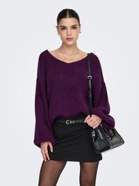 Maglione oversize viola in maglia con scollo ampio, abbinato a una minigonna nera e a una borsa nera testurizzata.